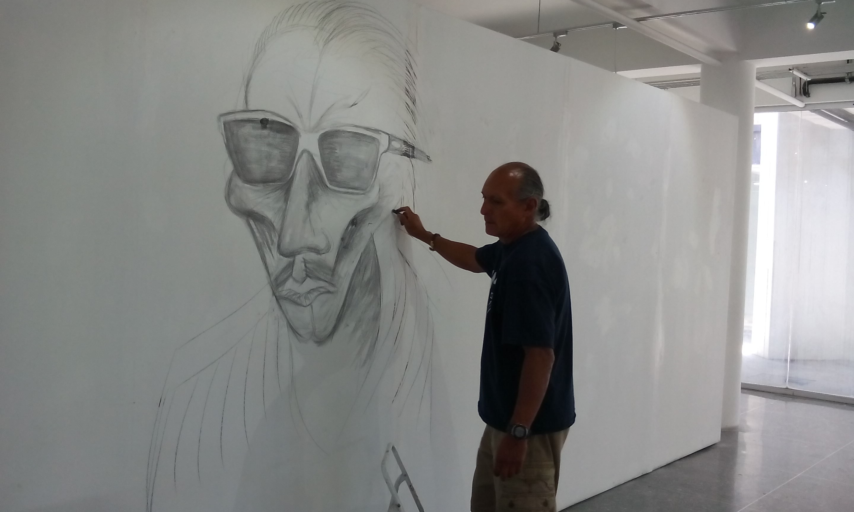 Large-scale self-portrait drawing — Ricardo Santos Hernández at work on the gallery wall, Museo de Arte de Nogales, Nogales, Sonora, Mexico. Created on-site for Urban Echo, a solo exhibition by Ricardo Santos Hernández, 2016. by Ricardo Santos Hernández