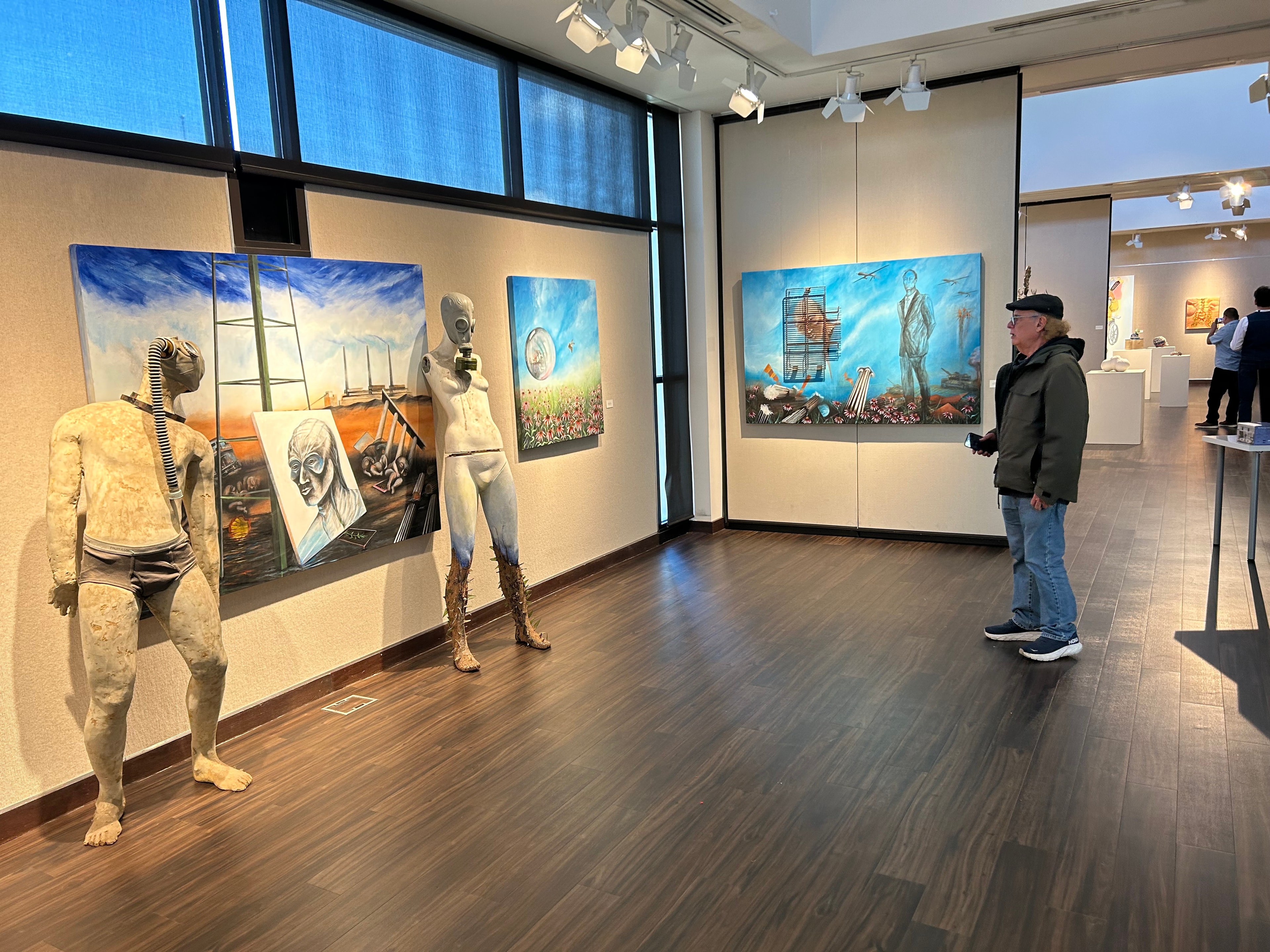 Christopher Gallery, ChingARTE — Rob Moore, the Chicago Blues Man, contemplates Ricardo's paintings at the Christopher Gallery, Prairie State College, Chicago Heights, IL. The large-scale mixed media works — sculptures and paintings in dialogue — fill the gallery walls. A quiet moment of connection between a musician and the visual world of resistance and identity. by Ricardo Santos Hernández