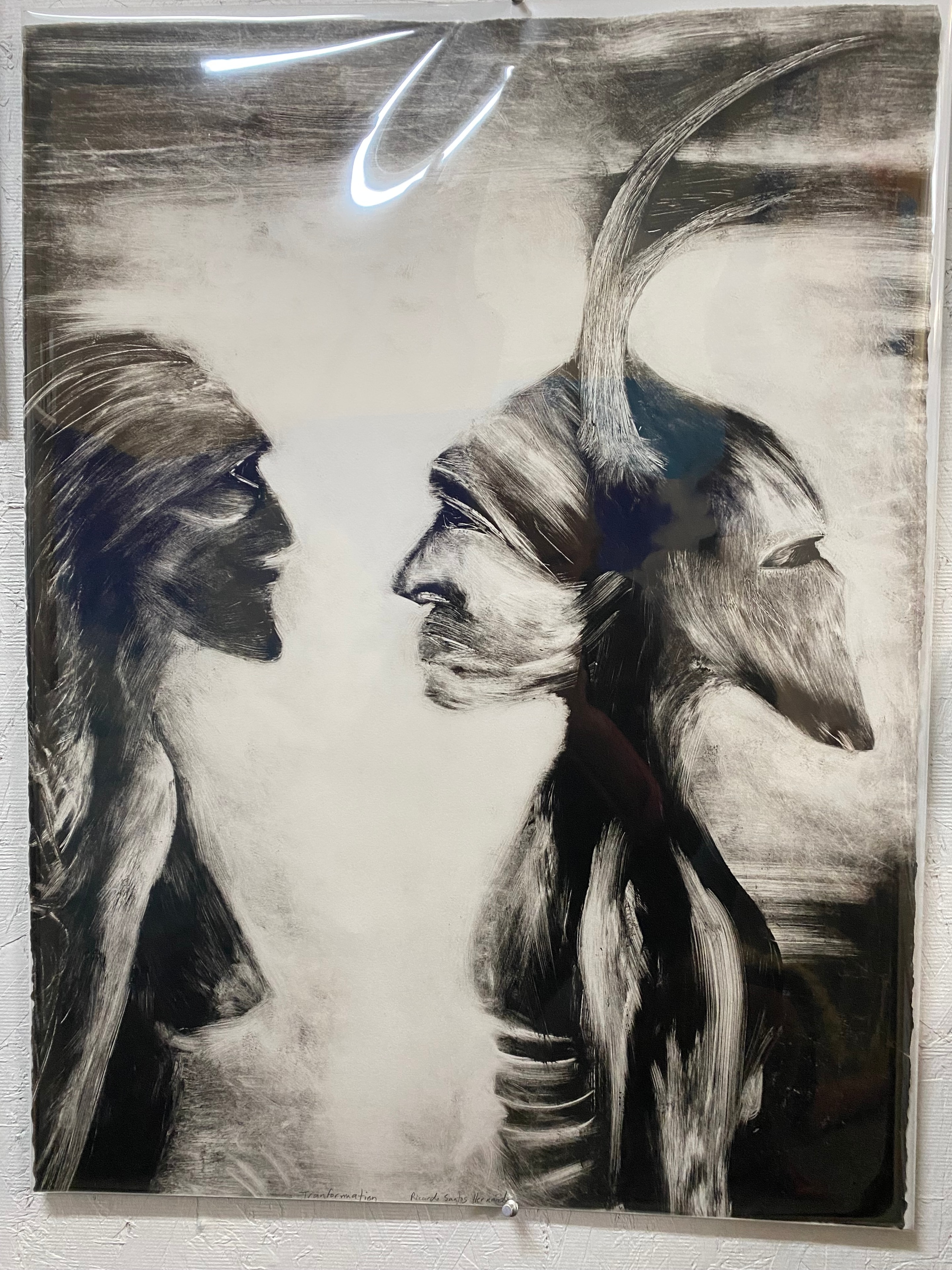 Transformation: I Mirror My Grandmother — Ricardo Santos Hernández. Monoprint. Printed at Hoof Print Chicago with Liz Borne and Gabe Hoar during a printing retreat in Wisconsin. Two faces meet at the center of the sheet — one above, one below, mirroring each other across a luminous white axis. The upper figure emerges from a field of dark, gestural brushstrokes; the lower answers in kind. They are the same face and different faces: Ricardo and his grandmother, separated by time and generation, joined in the act of looking. The monoprint process — ink pulled once from the plate, unrepeatable — makes the image itself an act of transformation. What is printed cannot be printed again. What is remembered cannot be remembered the same way twice. by Ricardo Santos Hernández